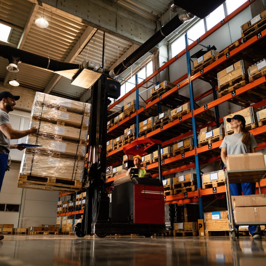 Low angle view of happy warehouse workers communicating while working with shipment in industrial storage compartment.